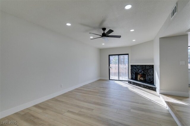 unfurnished living room with ceiling fan, a high end fireplace, and light wood-type flooring