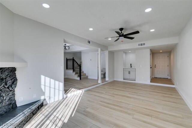 unfurnished living room with ceiling fan, light hardwood / wood-style flooring, and a stone fireplace