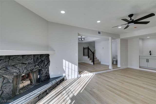 unfurnished living room featuring ceiling fan, sink, light hardwood / wood-style flooring, and a stone fireplace