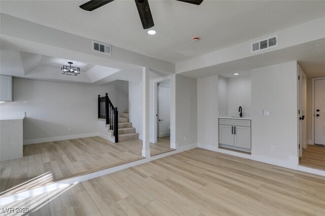 basement featuring sink, ceiling fan with notable chandelier, and light hardwood / wood-style flooring