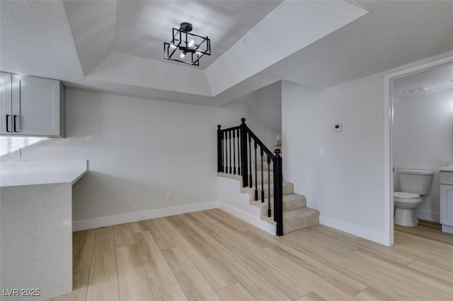 staircase with a textured ceiling, an inviting chandelier, hardwood / wood-style floors, and a tray ceiling