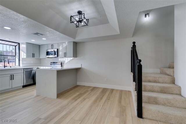 kitchen with kitchen peninsula, appliances with stainless steel finishes, light wood-type flooring, a textured ceiling, and a chandelier