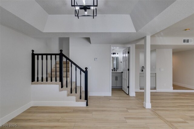 stairs featuring a raised ceiling, wood-type flooring, and a chandelier