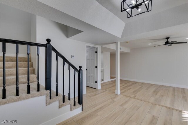 staircase featuring lofted ceiling, wood-type flooring, and ceiling fan with notable chandelier