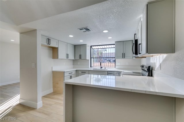 kitchen with gray cabinets, appliances with stainless steel finishes, kitchen peninsula, and sink