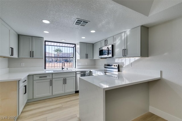 kitchen with sink, a textured ceiling, appliances with stainless steel finishes, and kitchen peninsula