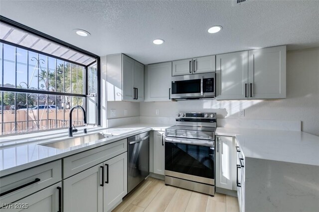 kitchen with light hardwood / wood-style floors, sink, gray cabinetry, stainless steel appliances, and a textured ceiling