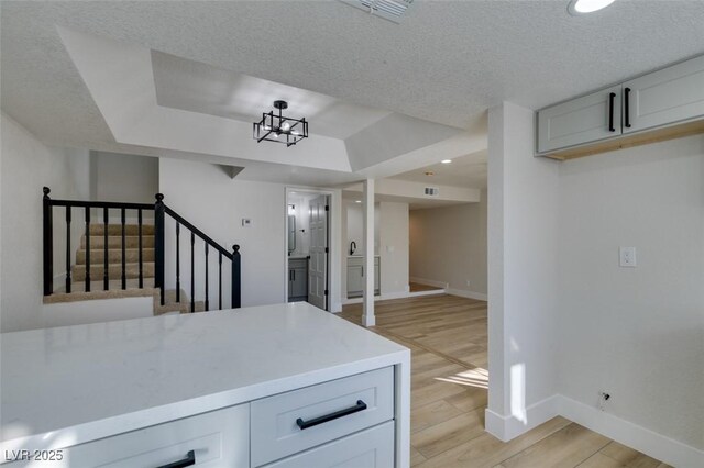 kitchen featuring a textured ceiling, a tray ceiling, white cabinetry, and light hardwood / wood-style floors