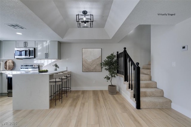 kitchen featuring a breakfast bar, kitchen peninsula, appliances with stainless steel finishes, and gray cabinets