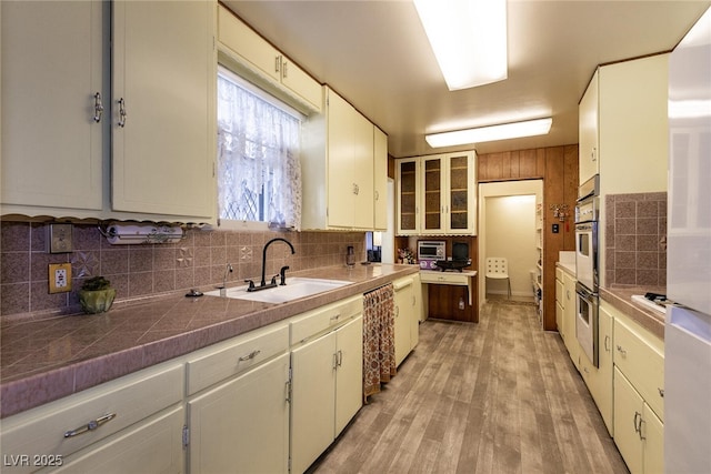 kitchen with dishwashing machine, sink, white cabinetry, and light hardwood / wood-style floors