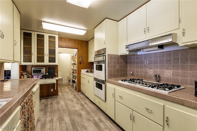 kitchen featuring backsplash, light hardwood / wood-style floors, white double oven, white cabinetry, and gas stovetop