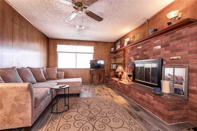 living room featuring ceiling fan, a fireplace, light hardwood / wood-style flooring, and wooden walls