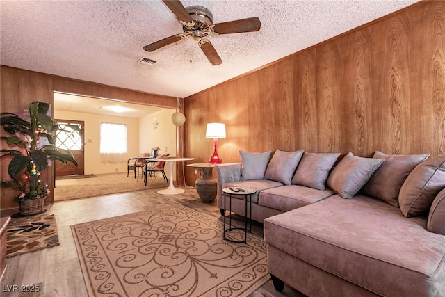 living room featuring a textured ceiling, ceiling fan, light hardwood / wood-style floors, and wooden walls