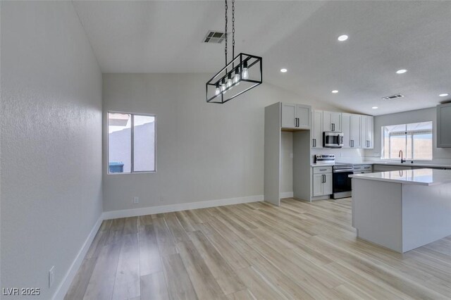 kitchen featuring light wood-type flooring, appliances with stainless steel finishes, hanging light fixtures, and gray cabinets