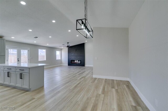 kitchen with decorative light fixtures, french doors, a fireplace, light wood-type flooring, and ceiling fan