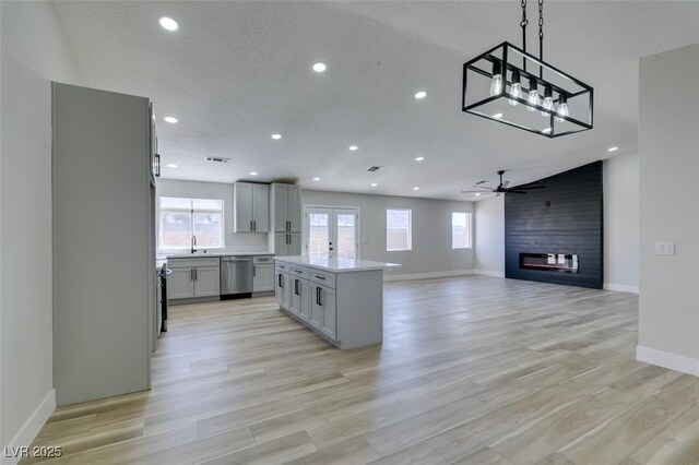 kitchen featuring a kitchen island, decorative light fixtures, a fireplace, stainless steel dishwasher, and gray cabinetry