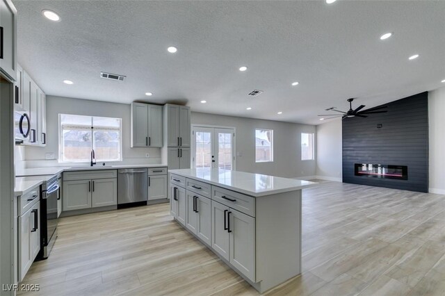 kitchen with light hardwood / wood-style floors, gray cabinets, ceiling fan, stainless steel appliances, and a fireplace