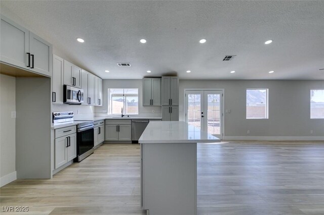 kitchen featuring light hardwood / wood-style floors, appliances with stainless steel finishes, french doors, a textured ceiling, and a center island