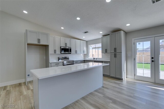 kitchen featuring appliances with stainless steel finishes, a kitchen island, french doors, sink, and light hardwood / wood-style flooring