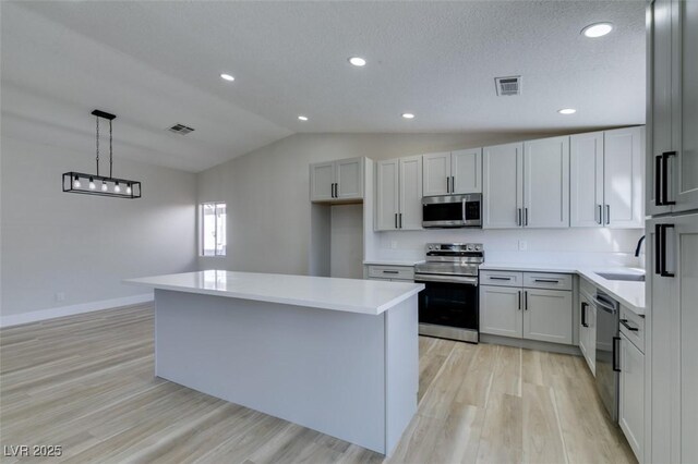 kitchen featuring light wood-type flooring, a center island, decorative light fixtures, stainless steel appliances, and vaulted ceiling