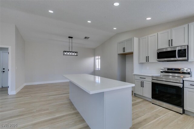 kitchen featuring a kitchen island, stainless steel appliances, light hardwood / wood-style floors, hanging light fixtures, and vaulted ceiling