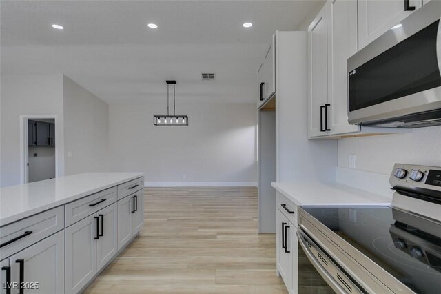 kitchen featuring white cabinetry, pendant lighting, appliances with stainless steel finishes, and light hardwood / wood-style flooring