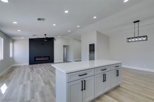 kitchen with ceiling fan, a fireplace, pendant lighting, white cabinets, and a center island