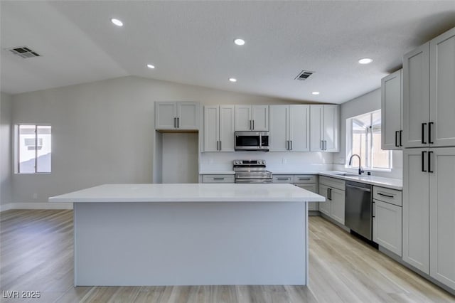 kitchen with light hardwood / wood-style floors, sink, stainless steel appliances, and a kitchen island