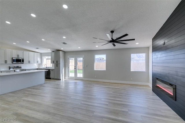 unfurnished living room featuring a fireplace, wood walls, sink, light wood-type flooring, and french doors