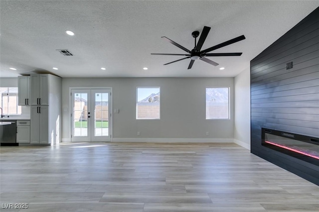 unfurnished living room with wood walls, a large fireplace, light wood-type flooring, a textured ceiling, and french doors