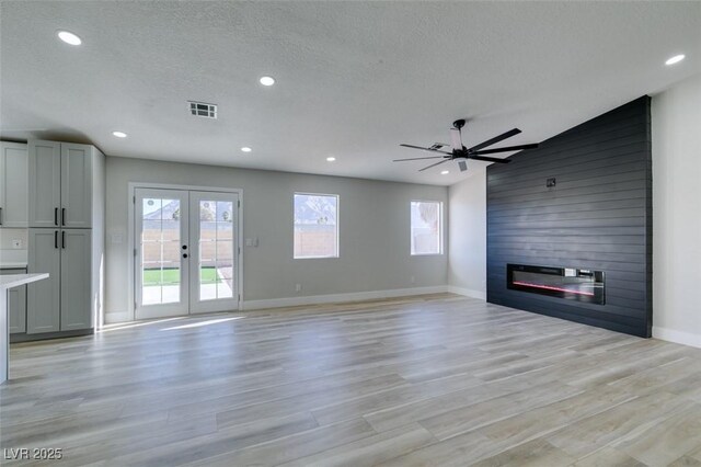 unfurnished living room featuring ceiling fan, a large fireplace, light hardwood / wood-style flooring, a textured ceiling, and french doors