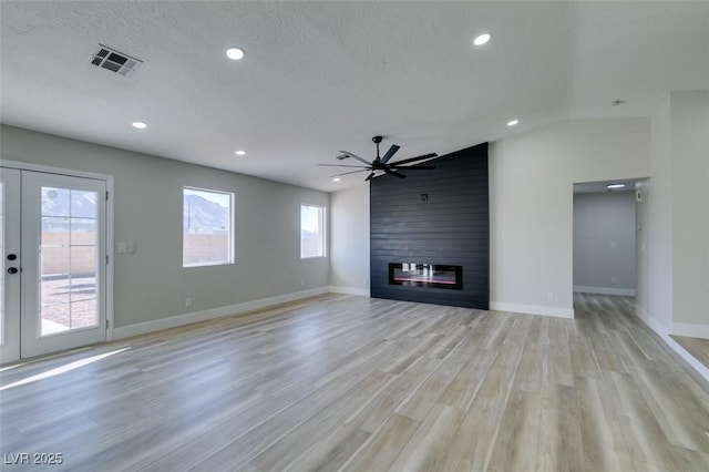 unfurnished living room with ceiling fan, light wood-type flooring, a large fireplace, french doors, and a textured ceiling