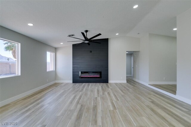 unfurnished living room featuring a textured ceiling, a large fireplace, vaulted ceiling, ceiling fan, and light hardwood / wood-style flooring