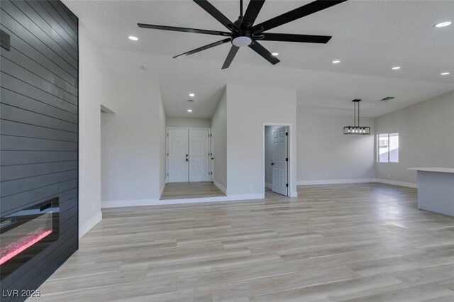 unfurnished living room with light wood-type flooring, ceiling fan, and a large fireplace