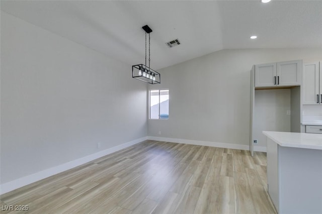 unfurnished dining area featuring vaulted ceiling and light hardwood / wood-style flooring