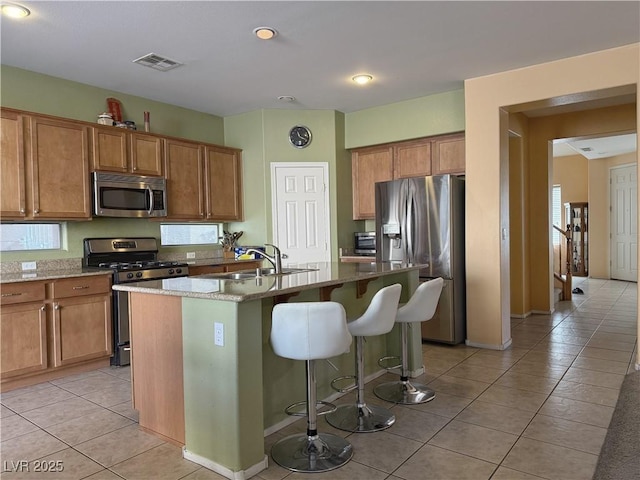 kitchen featuring light stone countertops, stainless steel appliances, an island with sink, sink, and light tile patterned floors