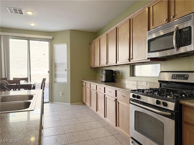 kitchen with light stone countertops, light tile patterned floors, stainless steel appliances, and sink