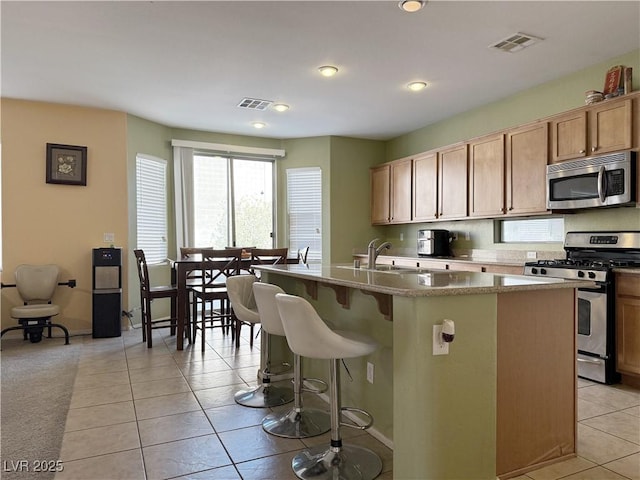 kitchen featuring a breakfast bar area, light tile patterned floors, a kitchen island with sink, and stainless steel appliances