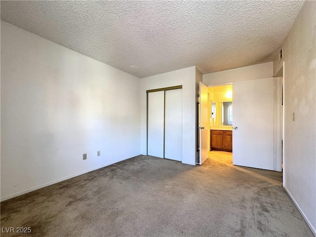 unfurnished bedroom featuring a textured ceiling, a closet, carpet floors, and ensuite bath