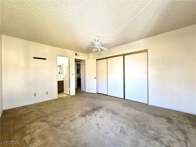 unfurnished bedroom with a textured ceiling, ensuite bath, carpet floors, a closet, and ceiling fan