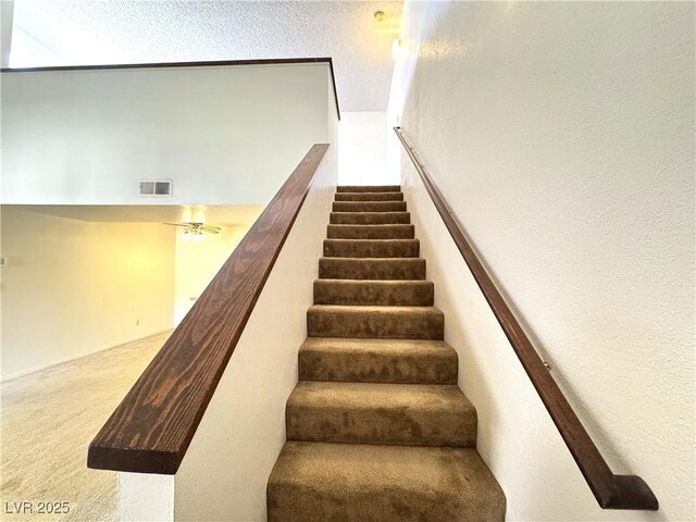 stairs featuring a textured ceiling and carpet flooring