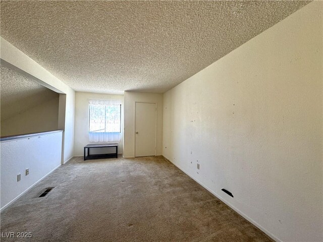 spare room with a textured ceiling, lofted ceiling, and carpet flooring