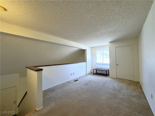 additional living space featuring light colored carpet and a textured ceiling