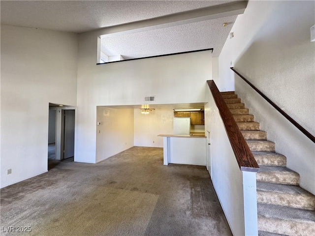 unfurnished living room with a textured ceiling, a towering ceiling, and carpet floors