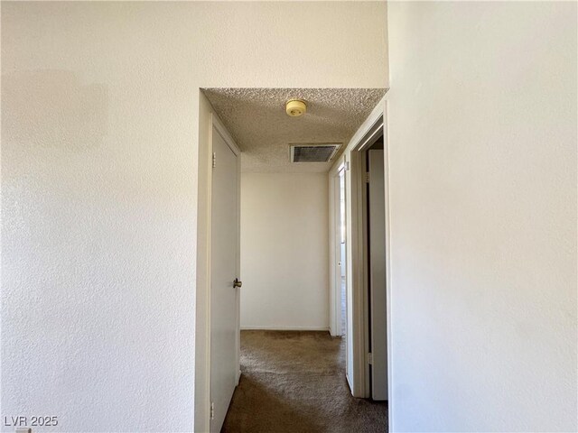 hall featuring a textured ceiling and dark colored carpet