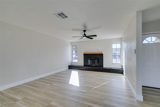 unfurnished living room featuring ceiling fan, light wood-type flooring, and a brick fireplace