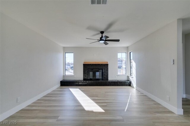 unfurnished living room with light wood-type flooring, ceiling fan, and a brick fireplace