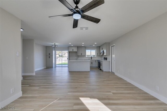 unfurnished living room featuring light wood-type flooring, ceiling fan, and sink