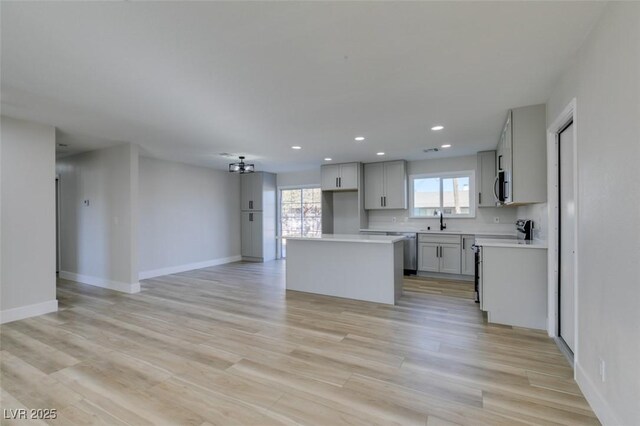 kitchen with a kitchen island, stainless steel appliances, sink, gray cabinets, and light hardwood / wood-style flooring