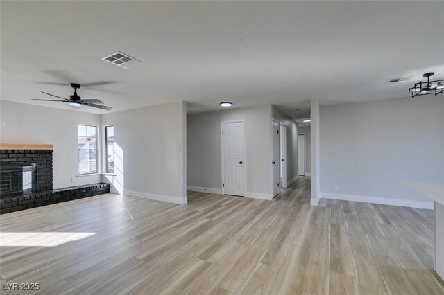 unfurnished living room featuring ceiling fan, a brick fireplace, and light hardwood / wood-style flooring